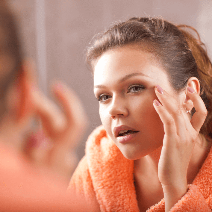 Ung kvinde iført orange badekåbe, der påfører make-up i spejlet.