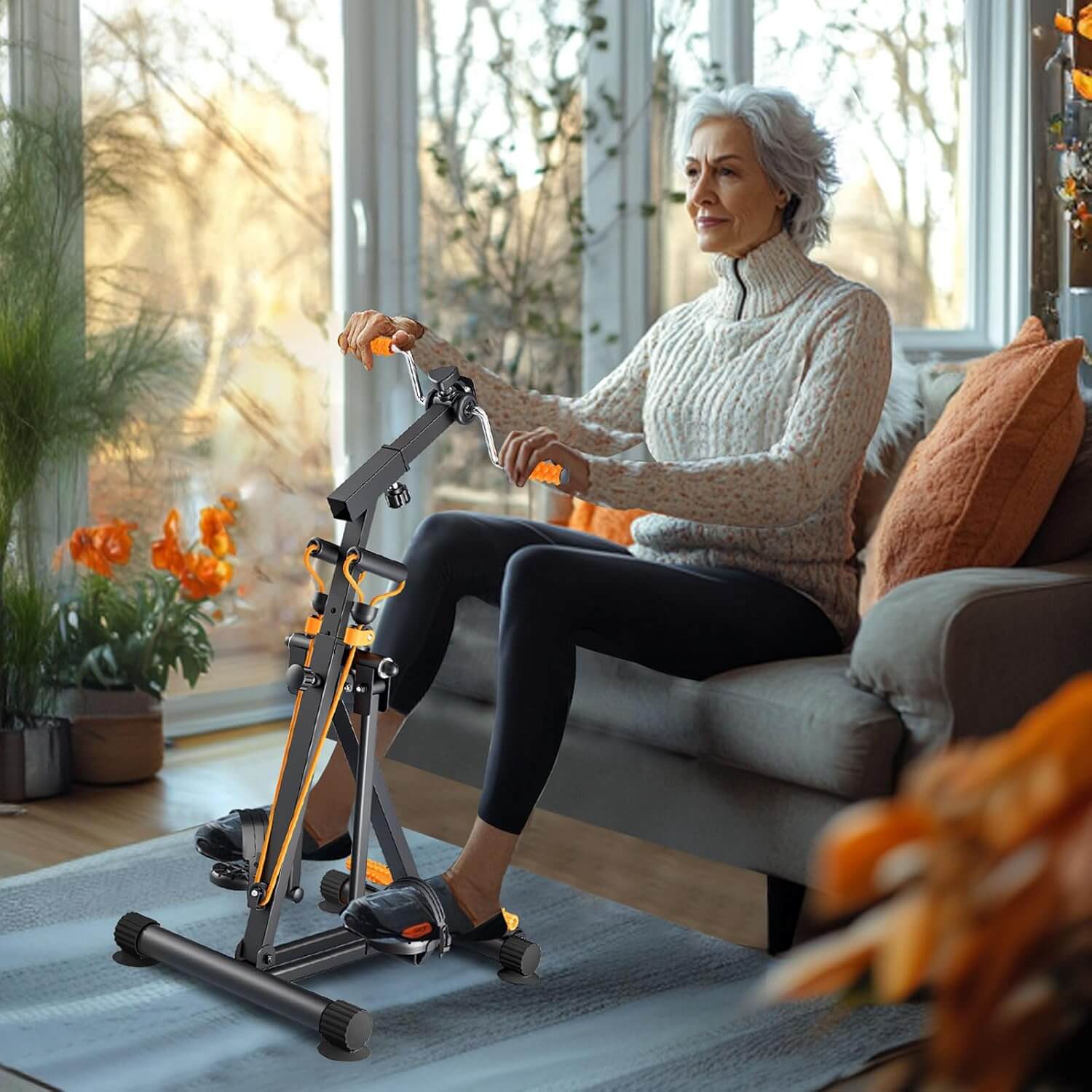 En ældre kvinde bruger SKÖNHED FlowCycle pedaltræner, mens hun sidder i en komfortabel stol med planter omkring.